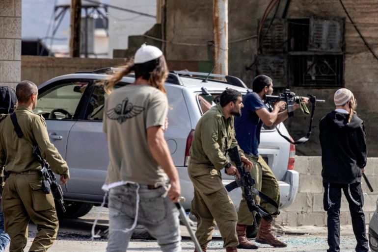 خبيران: التطهير بالضفة يستدعي محاكمة سموتريتش كمجرم حرب 1 Israeli settlers fire at Palestinians (unseen) while an Israeli soldier (L) stands by during clashes in the town of Huwara in the occupied West Bank on October 13, 2022. (Photo by Oren ZIV / AFP)