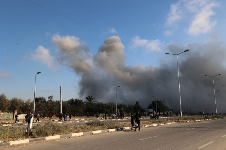 إسرائيل و"مؤسسة غزة".. العمل الإنساني في خدمة القتل 1 Smoke plumes rise during an Israeli strike as people walk along the Salah al-Din road near the Nusseirat refugee camp in the central Gaza Strip, used by food-seeking Palestinians to reach an aid distributution point set up by the privately-run Gaza Humanitarian Foundation (GHF), on June 25, 2025.