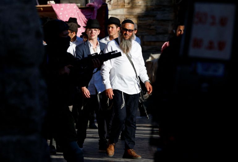 كيف حوّلت إسرائيل المستوطنين لمليشيا يحميها جيش الاحتلال؟ 2 Settlers look on as Israeli troops stand guard during a weekly settlers' tour in Hebron, in the Israeli-occupied West Bank July 19, 2025. REUTERS/Mussa Qawasma