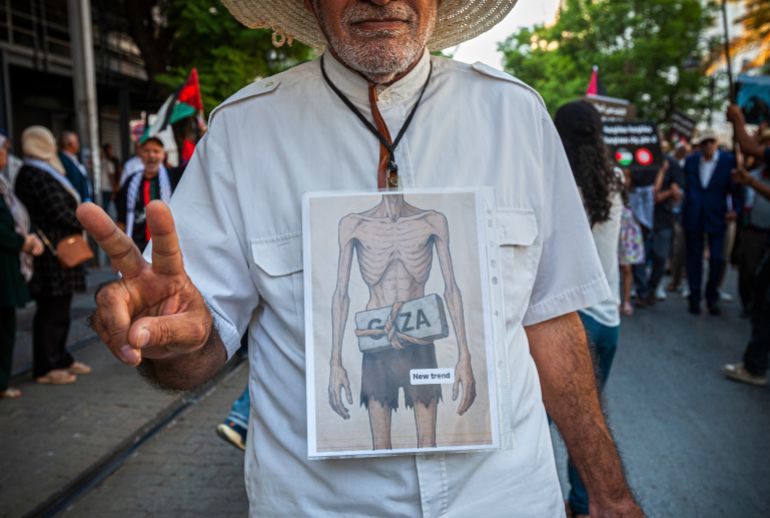 A protester wears a banner during a gathering calling for an end to Israel's war in the Gaza Strip and the starvation of Palestinian civilians, Sunday, Aug. 3, 2025, in Tunis, Tunisia. (AP Photo/Ons Abid)