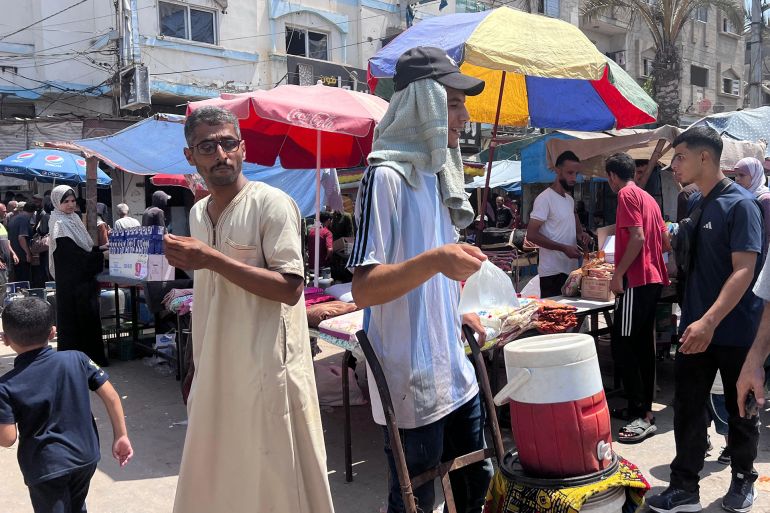 كيف يواجه الغزيون الحر الشديد وانقطاع الكهرباء في ظل الحرب؟ 2 شاب يبيع المياه المثلجة للمواطنين في سوق النصيرات (الجزيرة)