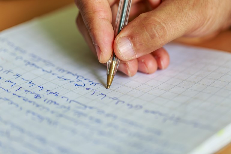 Arabic language writing a letter, a hand writes in Arabic with a blue pen