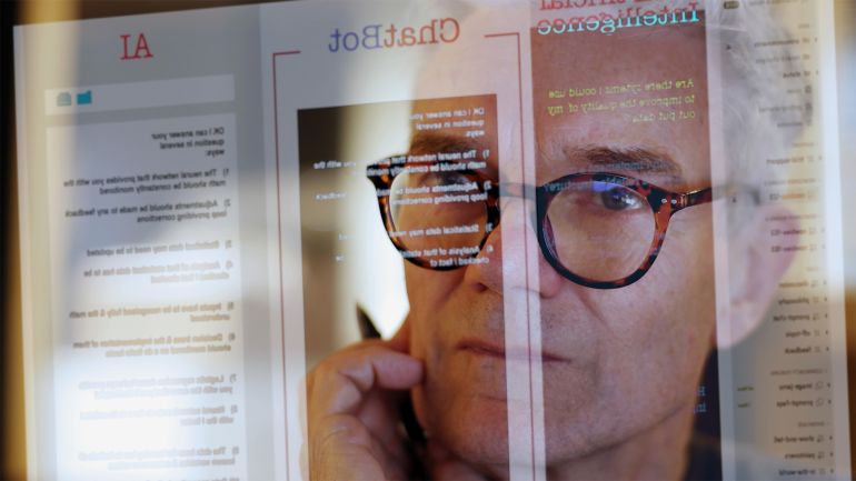 كيف يغير الذكاء الاصطناعي بيئة العمل الصحفي؟ 6 Close up stock photograph of a mature man studying a see-through computer monitor that’s displaying text provided by an AI (artificial intelligence) chatbot.