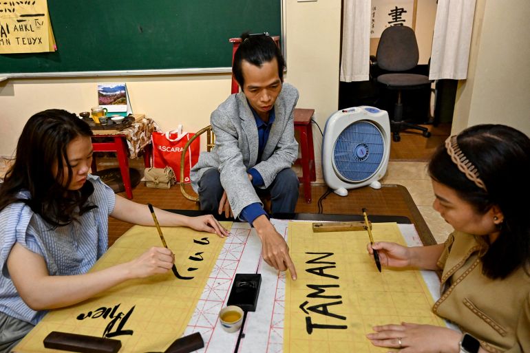 الكتابة بالأحرف اللاتينية موروث استعماري متجذر لدى الفيتناميين 1 This photo taken on May 15, 2025 shows calligrapher Nguyen Thanh Tung (C) teaching calligraphy to students at his home in Hanoi. At a calligraphy class in Hanoi, Hoang Thi Thanh Huyen slides her brush across the page to form the letters and tonal marks of Vietnam's unique modern script, in part a legacy of French colonial rule. (Photo by Nhac NGUYEN / AFP) / TO GO WITH VIETNAM-FRANCE-ALPHABET-DIPLOMACY-MACRON, FOCUS
