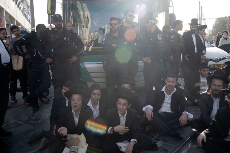 حملة لاعتقال الحريديم الفارين من الخدمة وقادتهم يهددون بإسقاط الحكومة 24 Israeli police stand guard as ultra-Orthodox Jewish men and boys, block a bus from crossing Jaffa Street in central Jerusalem, Thursday, Sept. 29, 2022 to protest attempts to force them to register for Israel's military draft. Military service is mandatory for most Jewish Israeli men, but the ultra-Orthodox often receive exemptions in order to continue their religious studies. (AP Photo/ Maya Alleruzzo)