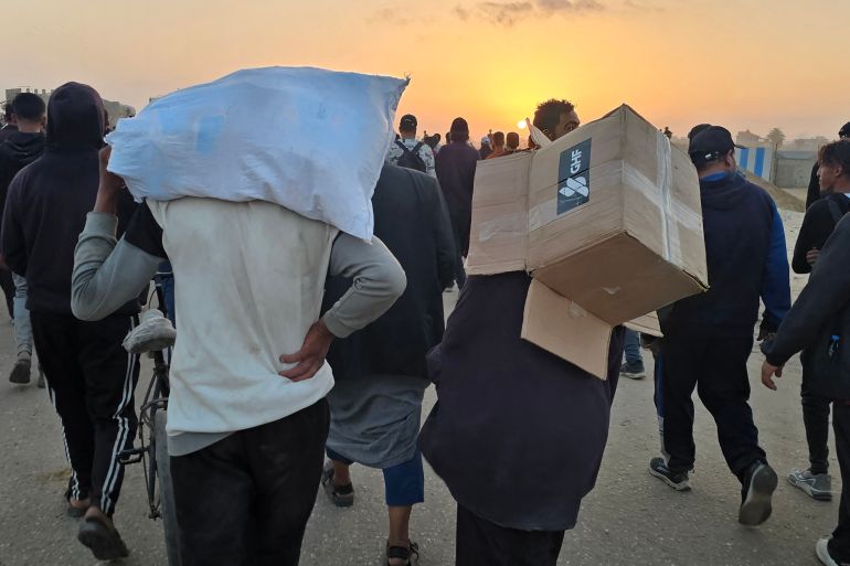 بالصور.. مساعدات غزة طرود مخضبة بالدماء 2 A youth carries an empty box of relief supplies from the Gaza Humanitarian Foundation (GHF), a private US-backed aid group that has bypassed the longstanding UN-led system in the territory, as displaced Palestinians walk near a food distribution centre in Rafah in the southern Gaza Strip on June 1, 2025. Gaza rescuers said Israeli gunfire killed at least 10 Palestinians and wounded more than 100 early on June 1, as thousands of people headed towards a US-backed aid distribution site. (Photo by AFP)