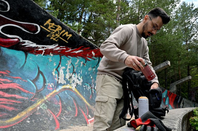 فن الشارع في سراييفو: جسور من الألوان في مواجهة الانقسامات القومية 2 Bosnian street artist Kerim Musanovic puts the finishing touches to his painting on the former Olympic bobsleigh track on Mount Trebevic, near Sarajevo, on May 26, 2025. (Photo by ELVIS BARUKCIC / AFP)